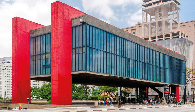 Museu de Arte de São Paulo (Masp) com imponente fachada de linhas retas no estilo arquitetônico modernista; em frente ao museu, há pessoas caminhando na calçada.