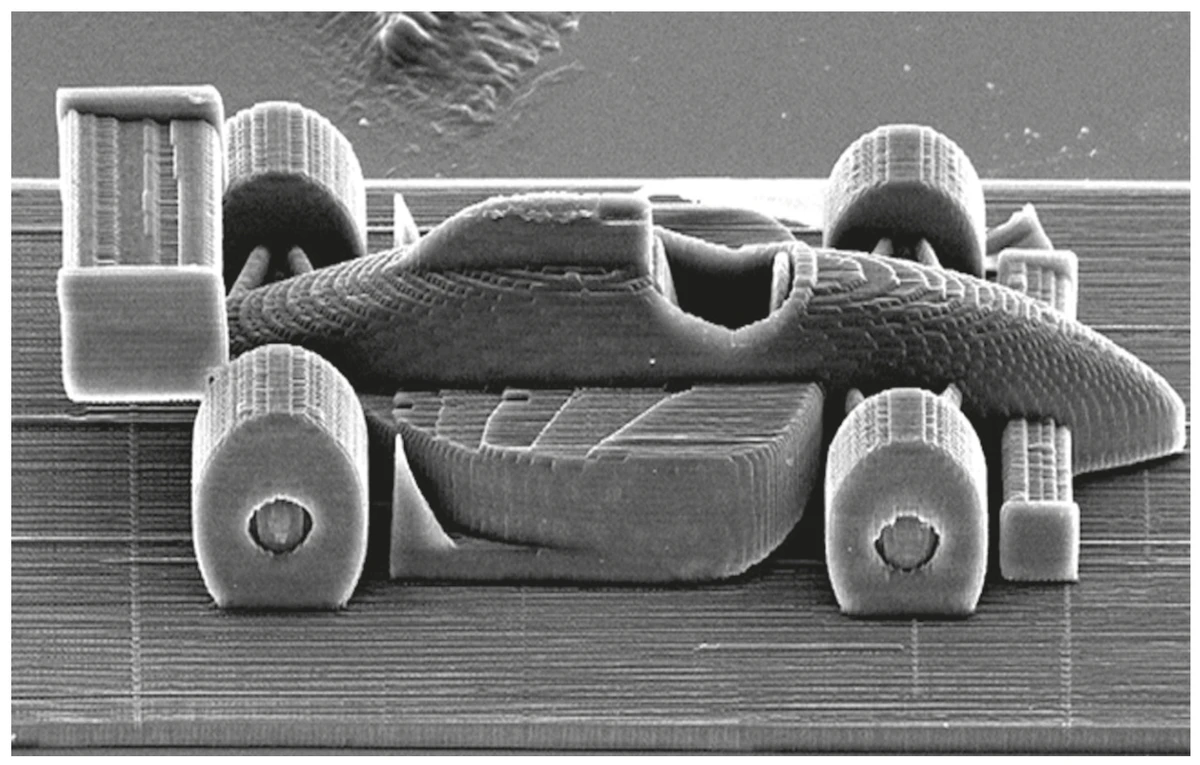 imagem ampliada de microscópio mostrando a escultura de um carro de Fórmula 1 impresso em resina, visto de lado, com as camadas da impressão 3D visíveis na carroceria e nas rodas