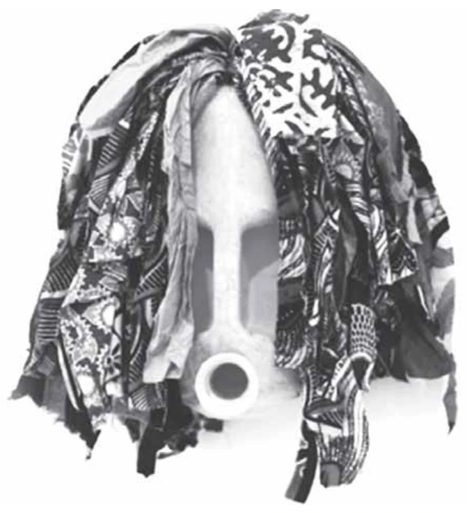fotografia em preto e branco de escultura em forma de máscara africana feita com um galão plástico de combustível cortado, cujo gargalo forma a boca, envolto por tiras de tecidos estampados que simulam uma cabeleira
