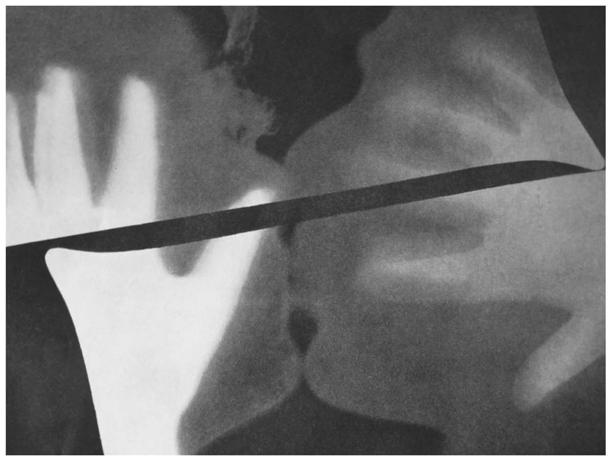 fotograma abstrato em preto e branco: silhuetas e sombras difusas de objetos sobrepostos, em tons de branco, cinza e preto, atravessadas por uma faixa escura reta na diagonal, sem qualquer figura reconhecível